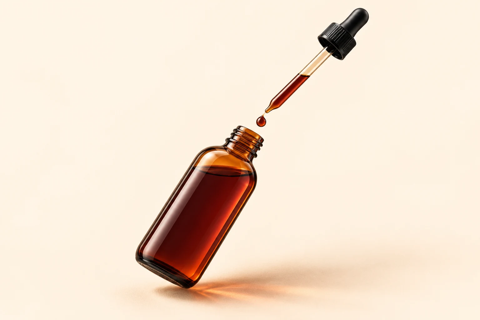 An unlabelled amber tincture bottle tilted beneath a slender glass pipette, with a drop of amber liquid suspended between them